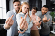 © LIGHTFIELD STUDIOS - Multicultural businesspeople on blurred background showing middle fingers in office
