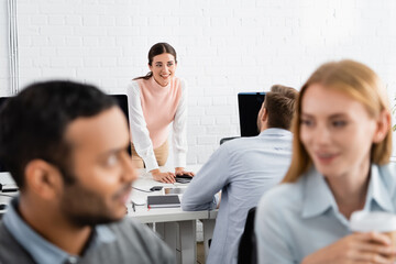 Smiling businesswoman looking at colleague near devices in office