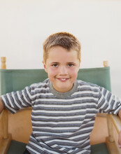 A Confident Boy Sitting In A Folding Director's Chair,smiling A Toothy Smile.