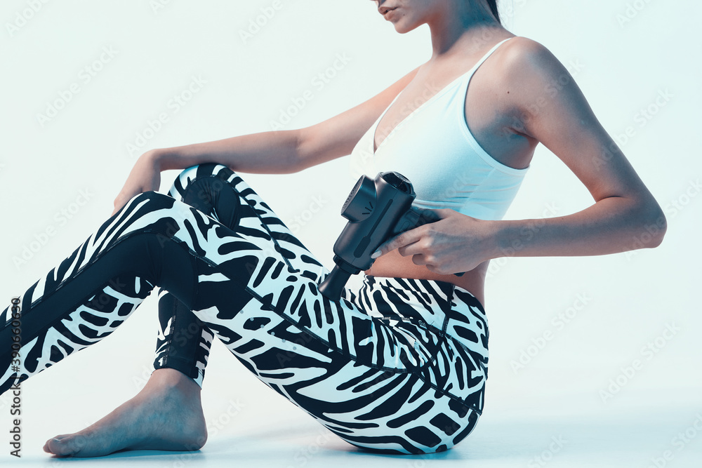 Sports young girl in sportswear massaging leg by massage gun in studio, pre-workout warm-ups, close up cropped ad photo - obrazy, fototapety, plakaty 