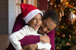 © fizkes - Close up African American man hugging adorable son wearing festive red cap, family celebrating Christmas, sitting near decorated tree at home, loving dad and little child boy cuddling, winter holiday