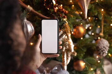 close up african american woman holding phone with empty white screen mockup near decorated festive 
