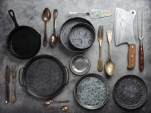 Old Vintage Tableware And Kitchen Utensils On Rustic Stone Background, Top View. Various Metallic Plates, Bowls, Cast-iron Pan, Cutlery. Set Of Assorted Antique Dish Ware, Kitchen And Cooking Concept