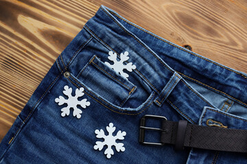 Blue classic jeans with pockets, belt and decorative wooden white snowflakes on the wooden surface.