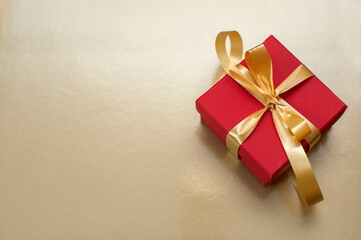 Red gift box with gold ribbon and bow on gold background