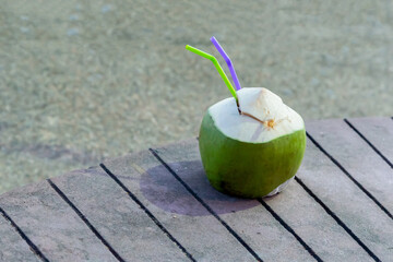 green coconut opened for access to milk liquid with two straws for a cocktail stands on a wooden table design topical drink