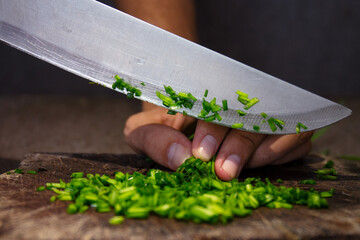 Wall Mural - Closeup shot of a man's hand slicing onion chives on a wooden chopping board