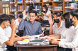 © THANANIT - Asian teacher raising hand and Giving Lesson to group of College Students for answer question in the library and classroom, University education, back to school after reopen Covid-19 outbreak concept