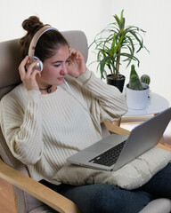 Wall Mural - Vertical shot of a young European woman using a laptop with headset sitting on the chair at home