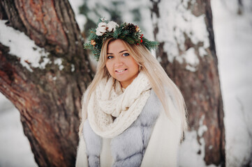 Portrait of a woman in a white fur coat in a cold winter forest. Girl with a wreath on her head in a snow-covered winter forest