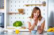© Dragana Gordic - Beautiful cute smiling woman is using smart phone on the kitchen at home. Young woman drinking first morning coffee and reading news in the kitchen of her apartment