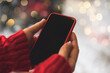 © Anna - Cropped of woman's hands in red sweater holding smartphone with blank screen of gadget at Christmas time. Digital mobile phone with copy space area