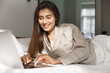© Liubov Levytska - Happy woman lying in bed with laptop and browsing internet. Girl relaxing and shopping online at home