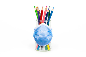 Color pencils in transparent glass jar with protective medical face mask isolated on white background. Concept of secured and safe art during quarantine and pandemic.