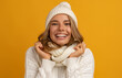 © mary_markevich - young smiling happy pretty blond woman wearing white knitted sweater, scarf and hat, warm winter cold season fashion accessories trend, posing on yellow studio background isolated