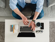 © mary_markevich - flat lay view from above on table workplace close-up man hands at home working typing on laptop online freelancer job, black empty screen, stationery