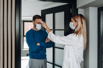 Wall Mural - Female doctor using infrared forehead thermometer to check patient's body temperature. They are wearing protective face masks. Pandemic, coronavirus (Covid-19) concept.