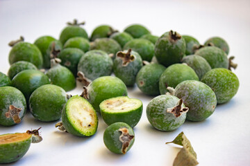 Large fleshy juicy Feijoa berries. Ripe dark green with sepals. A scattering of fruit on a light table. Whole and cut slices.