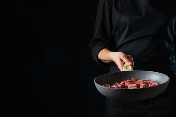 Chef holds frying pan with chopped raw meat on black background. Backstage of cooking grilled meat for dinner. Food concept. Frozen motion. Asian cuisine. Close-up view.