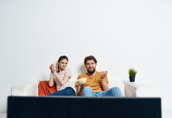 young man and woman watching tv with popcorn on sofa and red plaid green flower