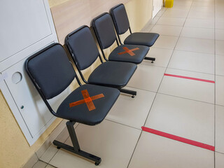 Four leather chairs in the hospital corridor. Red tape markers for social distancing in a pandemic