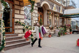 Fototapeta Kuchnia - Happy woman is holding gift box in her hands and smiling leaving the store. Beautiful happy girl posing with Christmas presents. New Year preparation