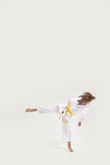 Full length shot of little karate girl in white kimono with a yellow sash exercising and fighting, doing martial arts, standing isolated over white background