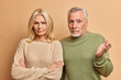 © WHstudio Leushin N - Self assured blonde middle aged woman stands with arms folded and looks seriously at camera her grey haired bearded husband shrugs shoulders in confusement being unaware. Family spouses indoor
