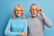 © WHstudio Leushin N - Cheerful middle aged woman and her husband pensioner reacts on shocking news keeps hand on spectacles isolated over blue background. Family age and emotions concept. Senior couple at pose home