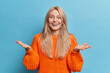 © wayhome.studio  - Cheerful unaware European woman spreads palms with bewilderment cannot believe in success stands indoor wears orange knitted sweater isolated over blue studio background. Human reactions concept