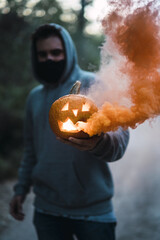 Sticker - Vertical shot of a man holding a carved pumpkin with an orange smoke - the concept of Halloween