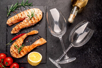 Dinner for two. Grilled salmon steaks, bottle of wine and glasses on stone background. View from above