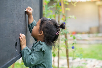 Wall Mural - Cute little girl writing alphabet on blackboard in garden.