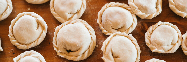 Wall Mural - pile of small homemade uncooked dumplings with meat on kitchen table. national traditional Russian cuisine. do it yourself. top view, flat lay. banner