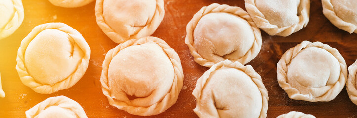 Wall Mural - pile of small homemade uncooked dumplings with meat on kitchen table. national traditional Russian cuisine. do it yourself. top view, flat lay. banner. flare