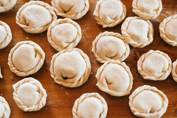 Wall Mural - pile of small homemade uncooked dumplings with meat on kitchen table. national traditional Russian cuisine. do it yourself. top view, flat lay