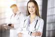© cameravit - Professional beautiful woman-doctor with a stethoscope is standing with crossed arms in a sunny clinic. Young doctors at work in a hospital. Medicine and healthcare concept
