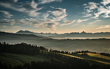 Wall Mural - overview swiss landscape with hills forests mountains in warm color during sunset or sunrise and epi