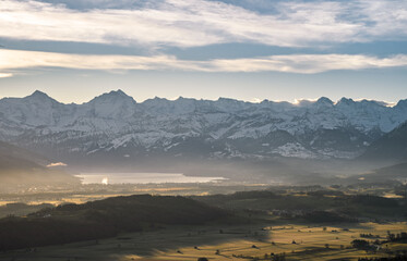 Wall Mural - overview swiss landscape with hills forests mountains in warm color during sunset or sunrise and epi