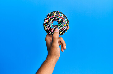 Canvas Print - Hand of hispanic man holding chocolate donut over isolated blue background.