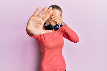 Poster - Beautiful caucasian woman wearing sportswear and arm band covering eyes with hands and doing stop gesture with sad and fear expression. embarrassed and negative concept.