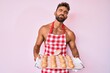 Young hispanic man shirtless wearing baker uniform holding homemade bread looking at the camera blowing a kiss being lovely and sexy. love expression.