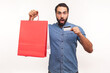 © khosrork - Extremely shocked bearded man holding and showing paper shopping bag and credit card looking at camera with excitement, great cashback, limitless card. Indoor studio shot isolated on white background