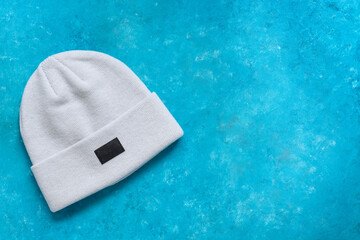 Knitted hat. Light gray modern knitted hat with label on a turquoise blue grunge background. Top view, flat lay, copy space.