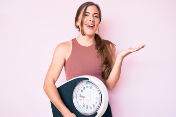 beautiful young caucasian woman holding weight machine to balance weight loss celebrating victory wi