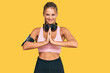 © Krakenimages.com - Young blonde woman wearing gym clothes and using headphones praying with hands together asking for forgiveness smiling confident.