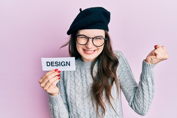 Wall Mural - Young beautiful caucasian girl holding design word on paper screaming proud, celebrating victory and success very excited with raised arm