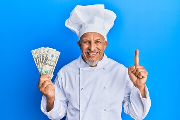 Sticker - Middle age grey-haired man wearing professional cook uniform holding usa dollars banknotes smiling with an idea or question pointing finger with happy face, number one