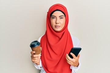 Wall Mural - Young beautiful hispanic girl wearing islamic hijab drinking a coffee usign smartphone skeptic and nervous, frowning upset because of problem. negative person.