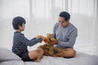 © khwanchai - Dad play bear doll with son on bed  in bedroom, relax and family time concept